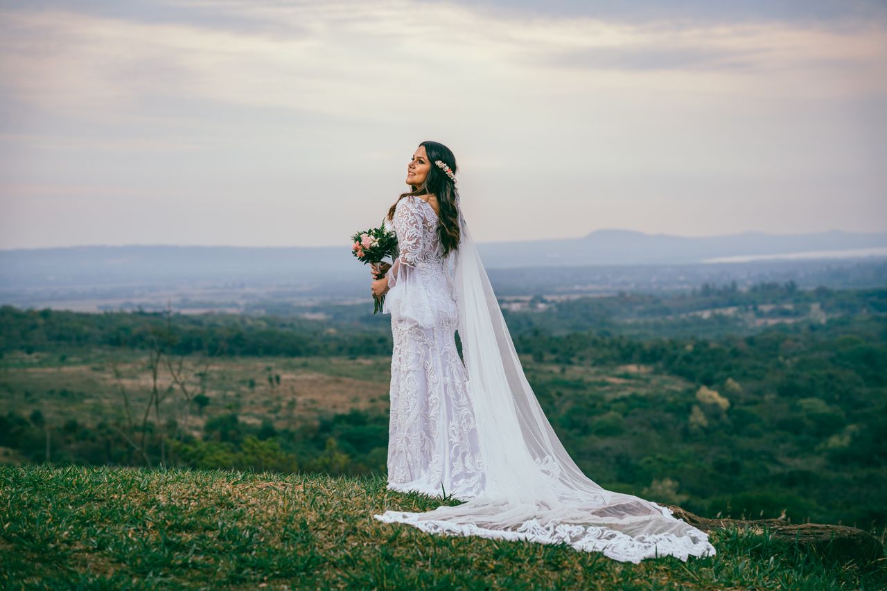 About Bride in elegant wedding dress posing on Caacupé hillside at sunset.