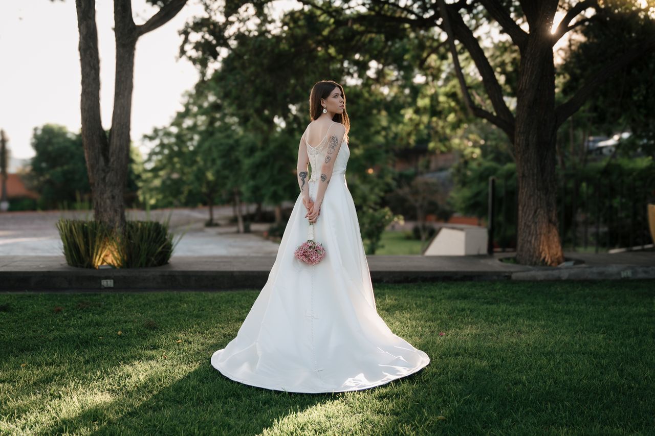 About Bride in an elegant wedding dress holds a bouquet, standing gracefully in a park setting.