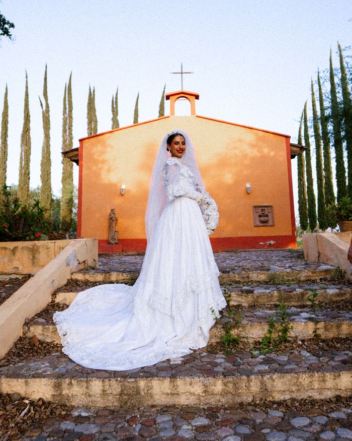About Bride in traditional wedding dress stands before colorful chapel in Mexico.