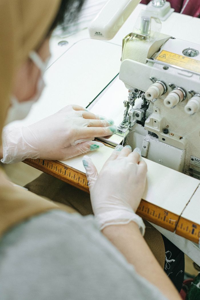 Close-up of a person sewing with a machine in a workshop, hands in gloves.