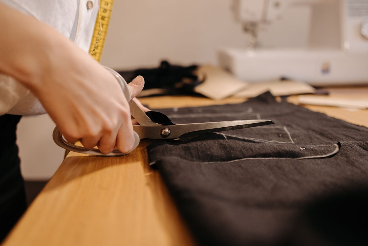 Contact A seamstress cuts black fabric with scissors, showcasing tailoring expertise.