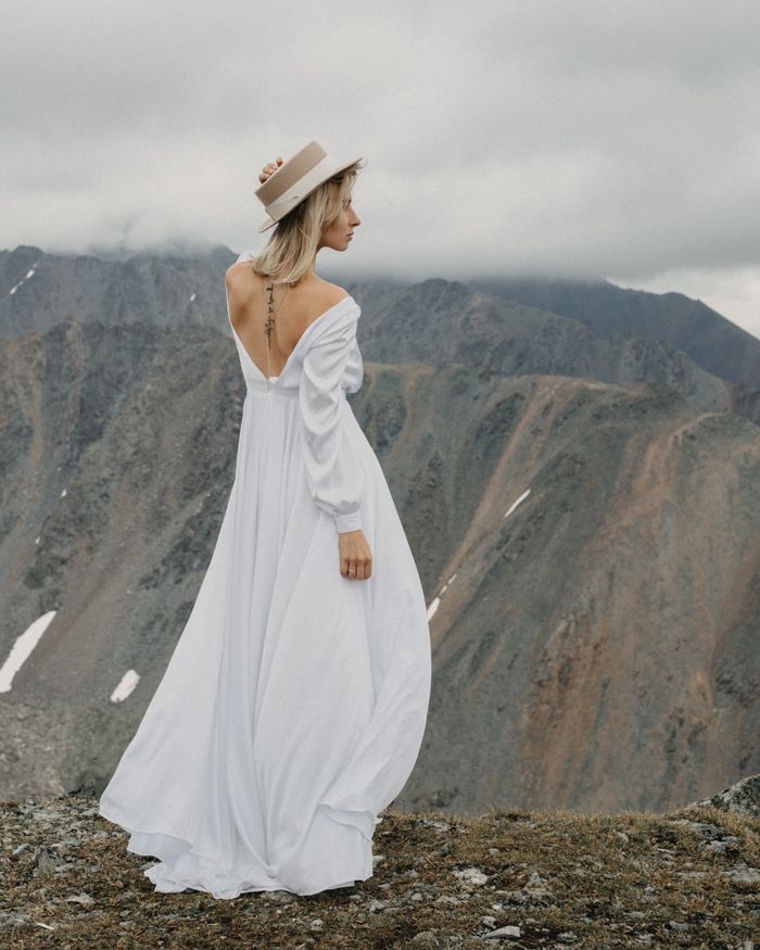 About Back view of tender female in bridal dress and hat admiring majestic mountain with snow on wedding day