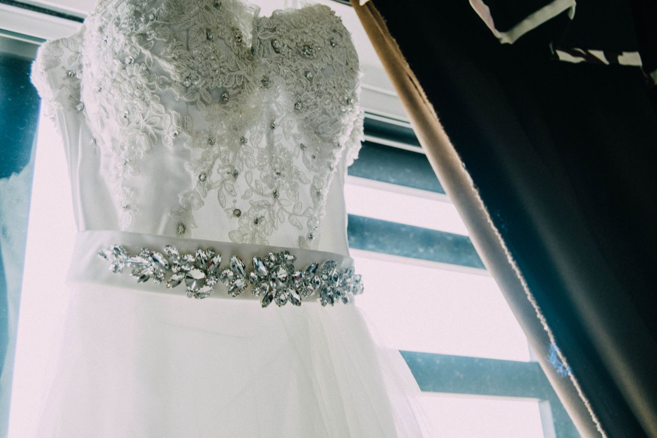 Contact A close-up of an elegant lace wedding dress featuring intricate beading and a shimmering belt.